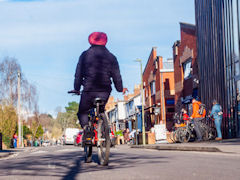 Low angle rear view of cyclist in helmet in centre of quiet residential street on sunny day