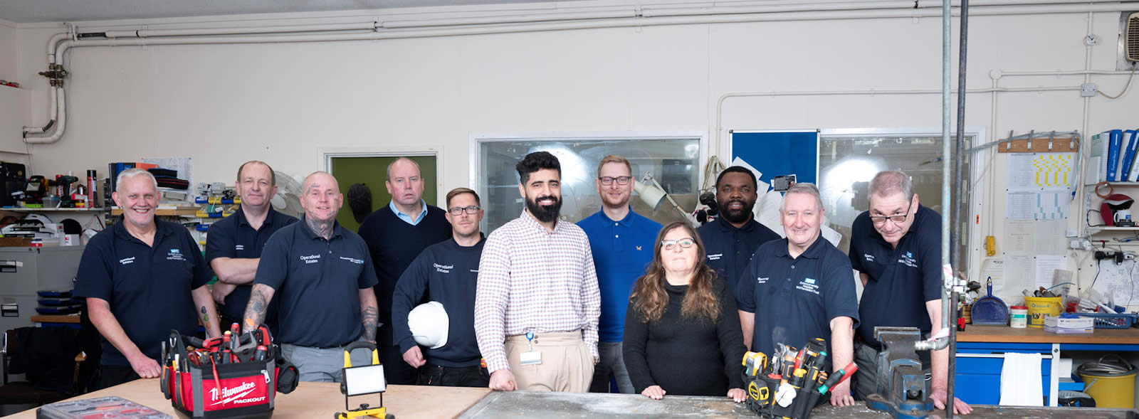 10 smiling men and one woman in workwear lined up at a workship table