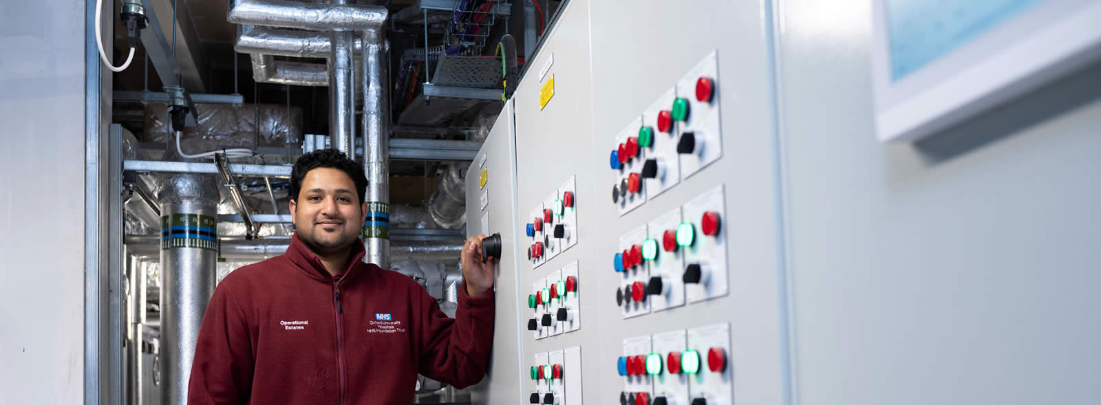 Smiling man of colour in work fleece standing by panel with large buttons, in a trunk room